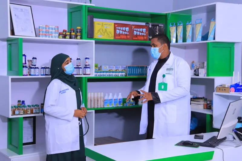 Two clinicians discussing treatment beside the clinic's herbal shelves
